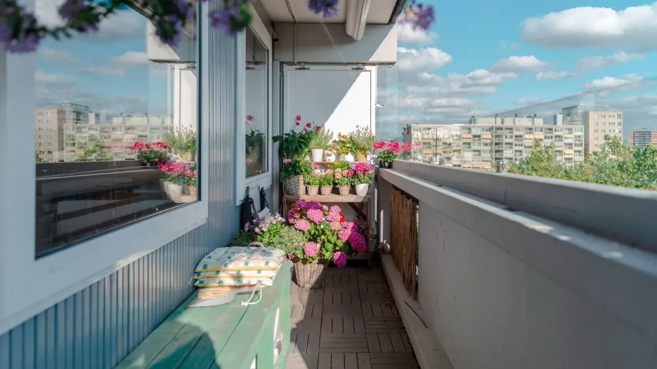 Uroczy balkon z drewnianą podłogą, zieloną ławką i mnóstwem kwiatów. Idealne miejsce, by odpocząć, gdy szukasz pomysłów, co na balkon zamiast płytek.