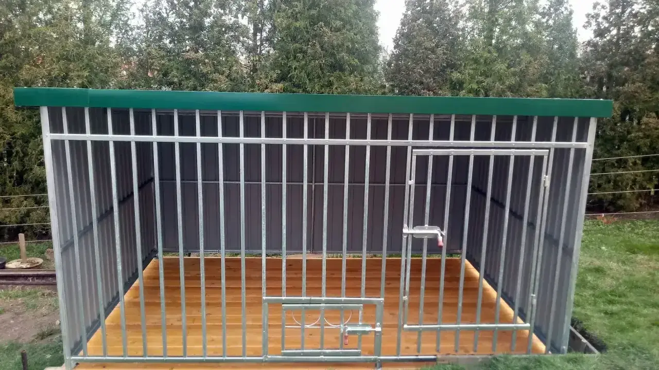 Solidny kojec dla psa z paneli ogrodzeniowych, z drewnianą podłogą i zielonym dachem. Idealne miejsce dla czworonoga.