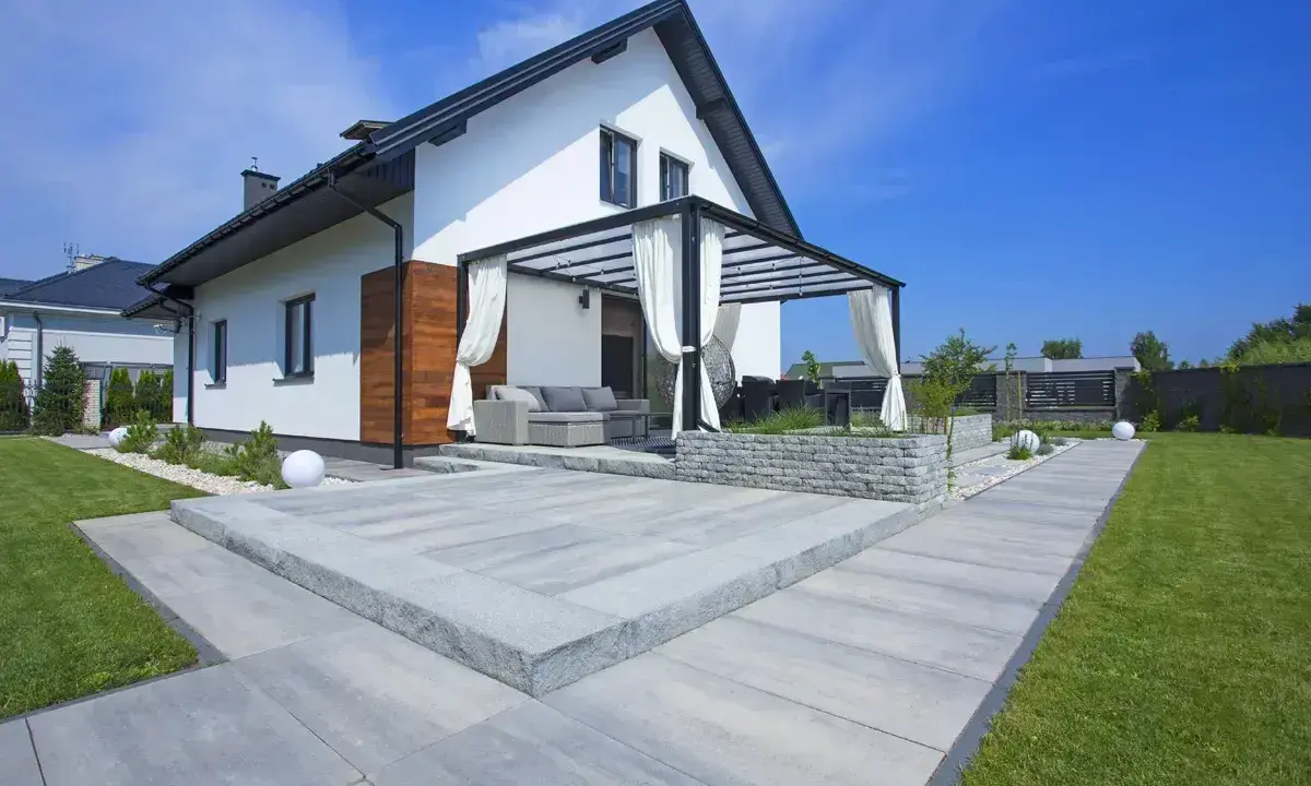 Nowoczesny taras z szarego betonu, z pergolą i meblami ogrodowymi. Idealne miejsce na relaks.