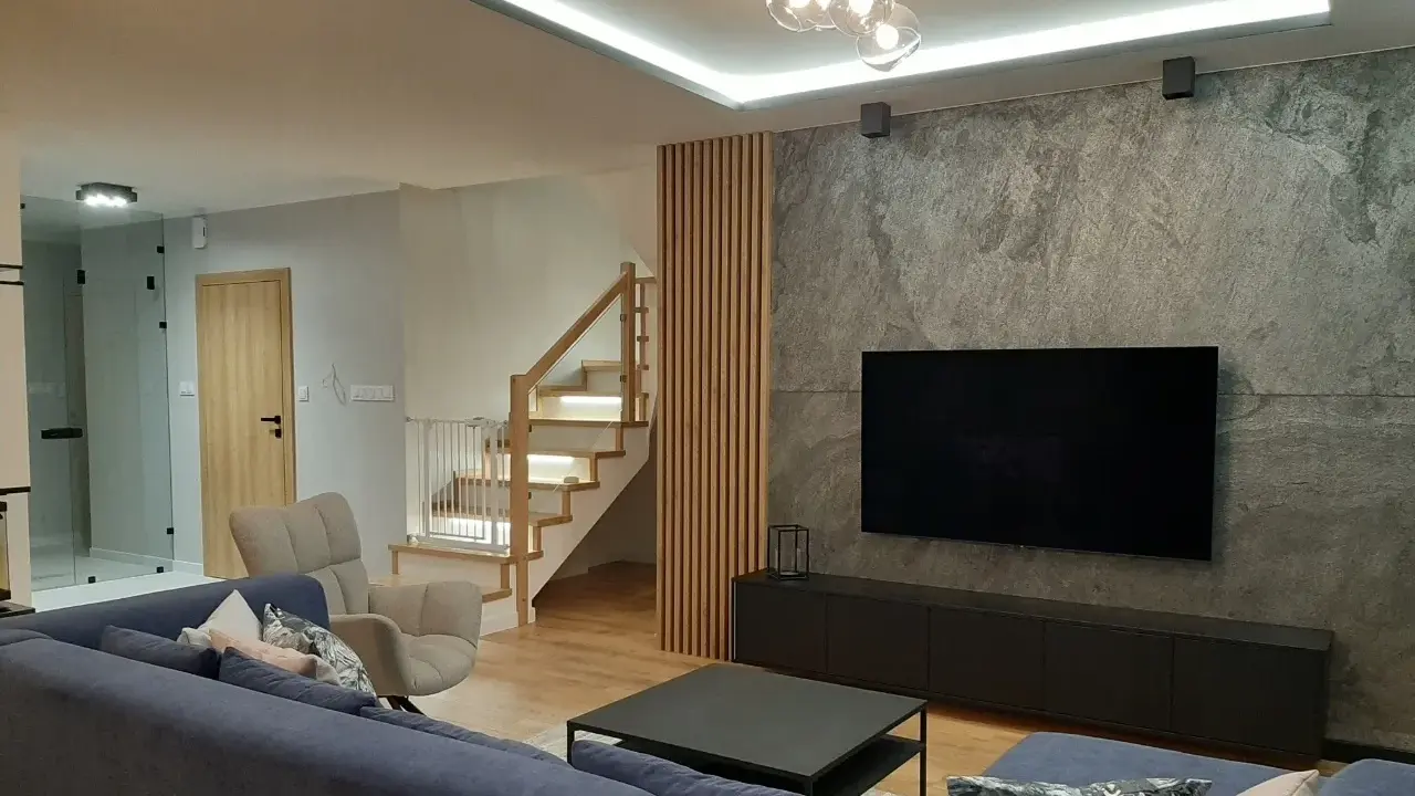 Nowoczesny salon z szarą ścianą, telewizorem i drewnianymi lamelami. Zobacz, z czym łączyć lamele, by stworzyć przytulne wnętrze.