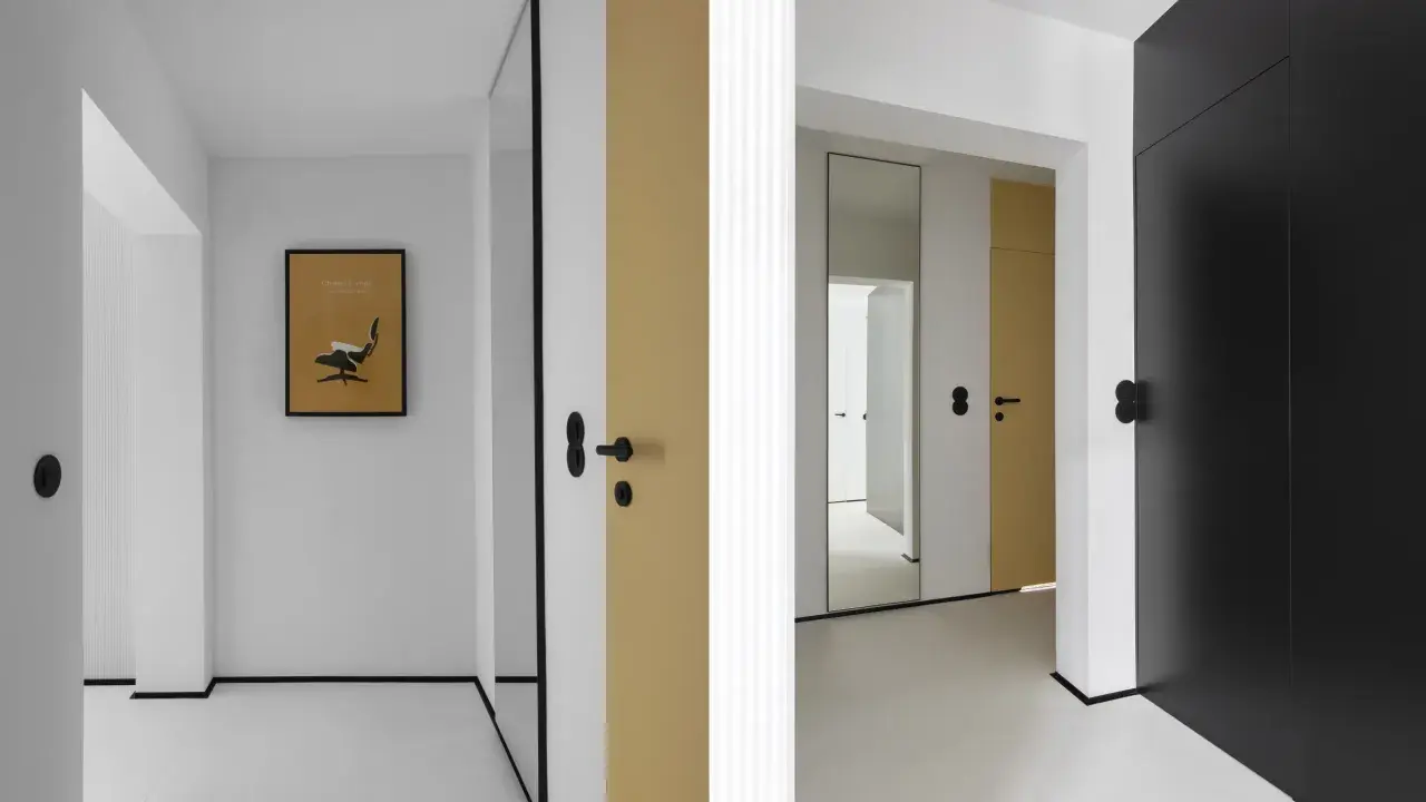 Minimalistyczny, mały przedpokój inspiracje ściany: złote i czarne drzwi, lustro, grafika z fotelem Eamesa.