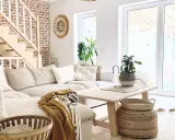Jasny salon w stylu boho z beżową kanapą, drewnianymi schodami i ceglaną ścianą.