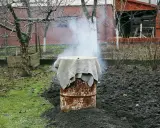 Dym unosi się z beczki, która służy jako prowizoryczna wędzarnia. Wokół niej widać ziemię i trawę.