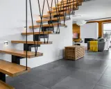Nowoczesne schody w domu z drewnianymi stopniami i czarną balustradą, oświetlone dyskretnymi kinkietami.