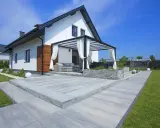 Nowoczesny taras z szarego betonu, z pergolą i meblami ogrodowymi. Idealne miejsce na relaks.