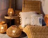 Przytulny balkon w stylu boho z wiklinowymi latarenkami, poduszkami i leżakiem.