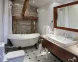 Mała łazienka w stylu retro z wanną na nóżkach, kamienną ścianą i drewnianymi belkami. Urokliwe wnętrze z nowoczesnymi akcentami.