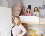 Uśmiechnięte dziewczynki w pokoju dla rodzeństwa, ozdobionym gwiazdkami i księżycem. Obok łóżka piętrowego stoi kobieta.