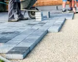 Układanie betonowych płyt na żwirze. Pracownicy tworzą ścieżkę, gdzie beton zamiast kostki staje się nowoczesnym rozwiązaniem.