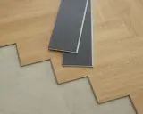 Panele winylowe w trakcie układania na betonowej podłodze. Dwa szare panele leżą na drewnianych deskach, pokazując, jak układać panele winylowe.