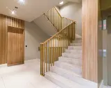 Drewniane lamele i nowoczesna klatka schodowa z metalową balustradą. Idealne inspiracje, co położyć na ściany na klatce schodowej.
