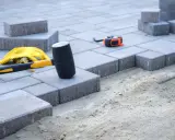 Beton pod kostkę czeka na ułożenie. Młotek gumowy, rękawice i miarka gotowe do pracy.