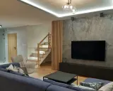 Nowoczesny salon z szarą ścianą, telewizorem i drewnianymi lamelami. Zobacz, z czym łączyć lamele, by stworzyć przytulne wnętrze.