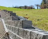 Budowa muru oporowego z bloczków betonowych, z drabiną i sznurkiem do poziomowania.