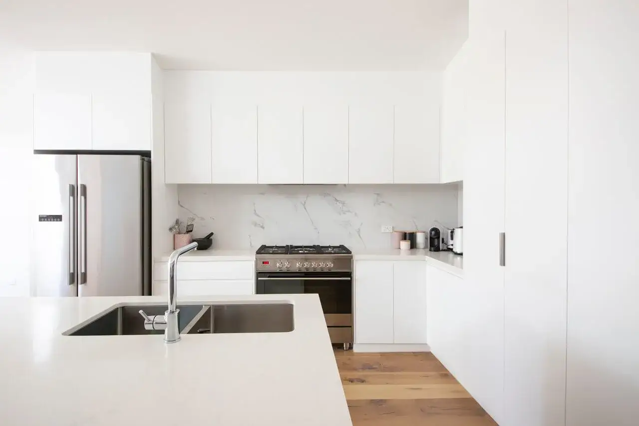 Nowoczesna, biała aranżacja małej kuchni 2m2 z lodówką, płytą grzewczą i wyspą ze zlewem.