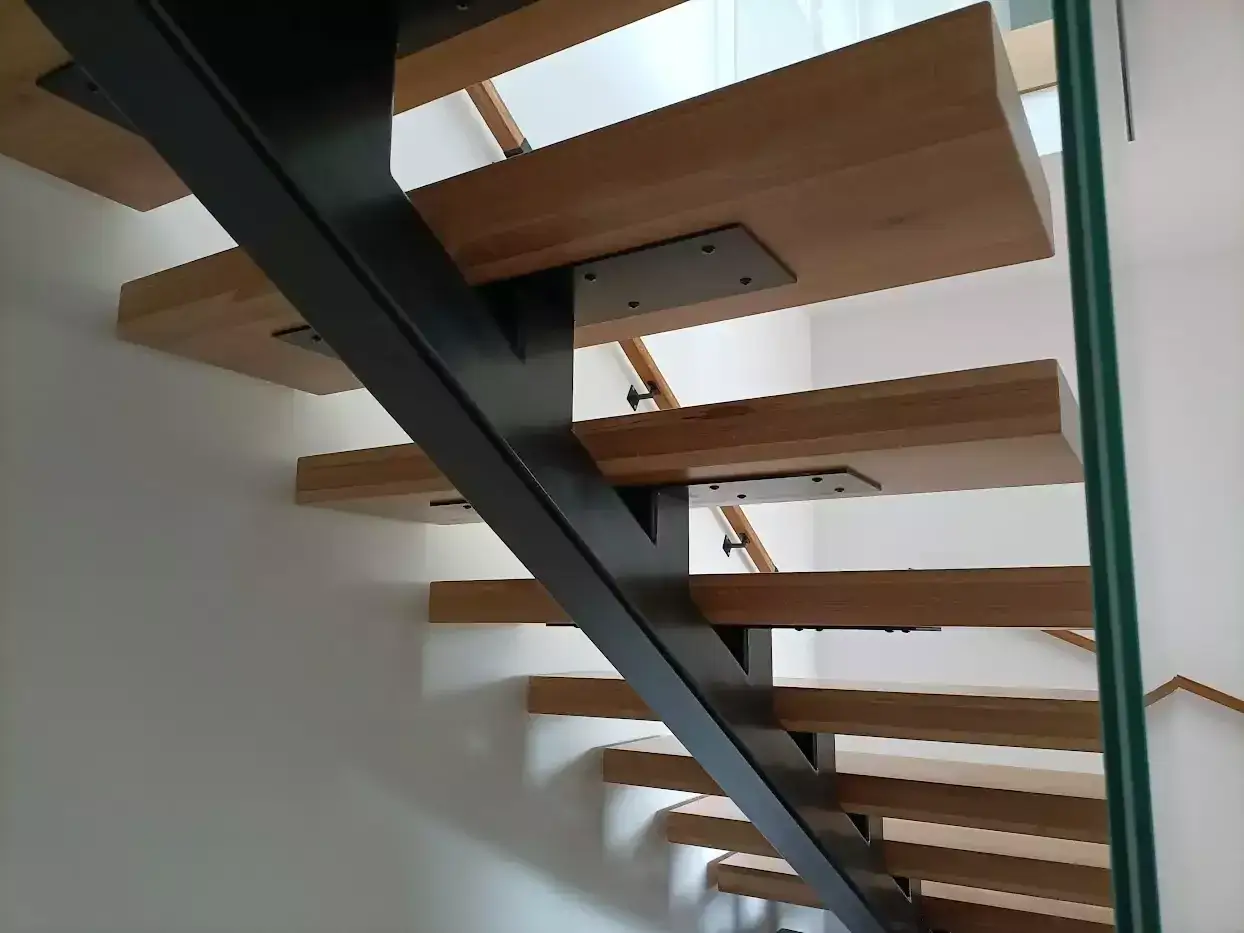 Nowoczesne schody wewnętrzne z drewnianymi stopniami i czarną, metalową konstrukcją. Świetny pomysł na schody wewnętrzne, dodają lekkości i stylu.