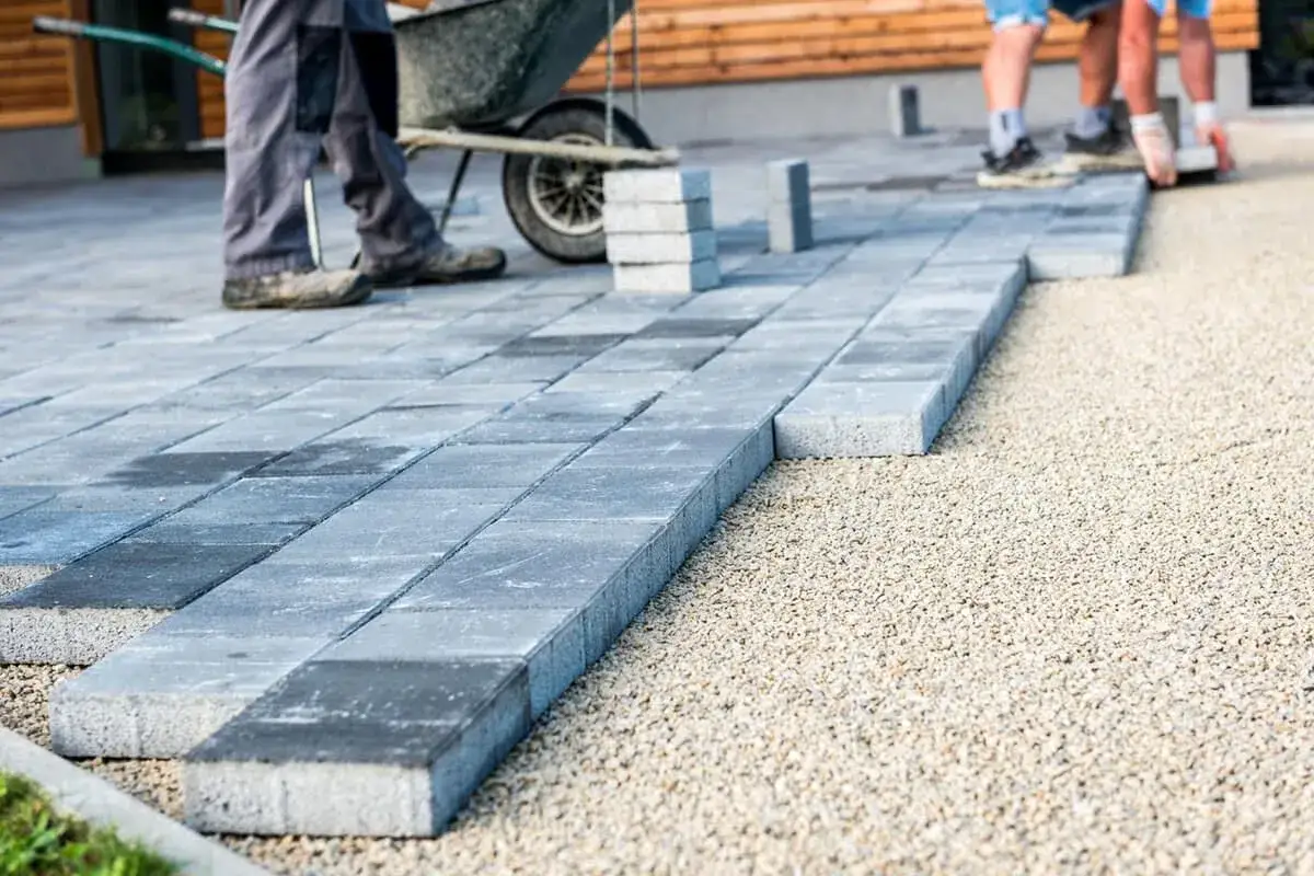 Układanie betonowych płyt na żwirze. Pracownicy budowlani tworzą nową nawierzchnię, gdzie beton zamiast kostki stanowi nowoczesne rozwiązanie.