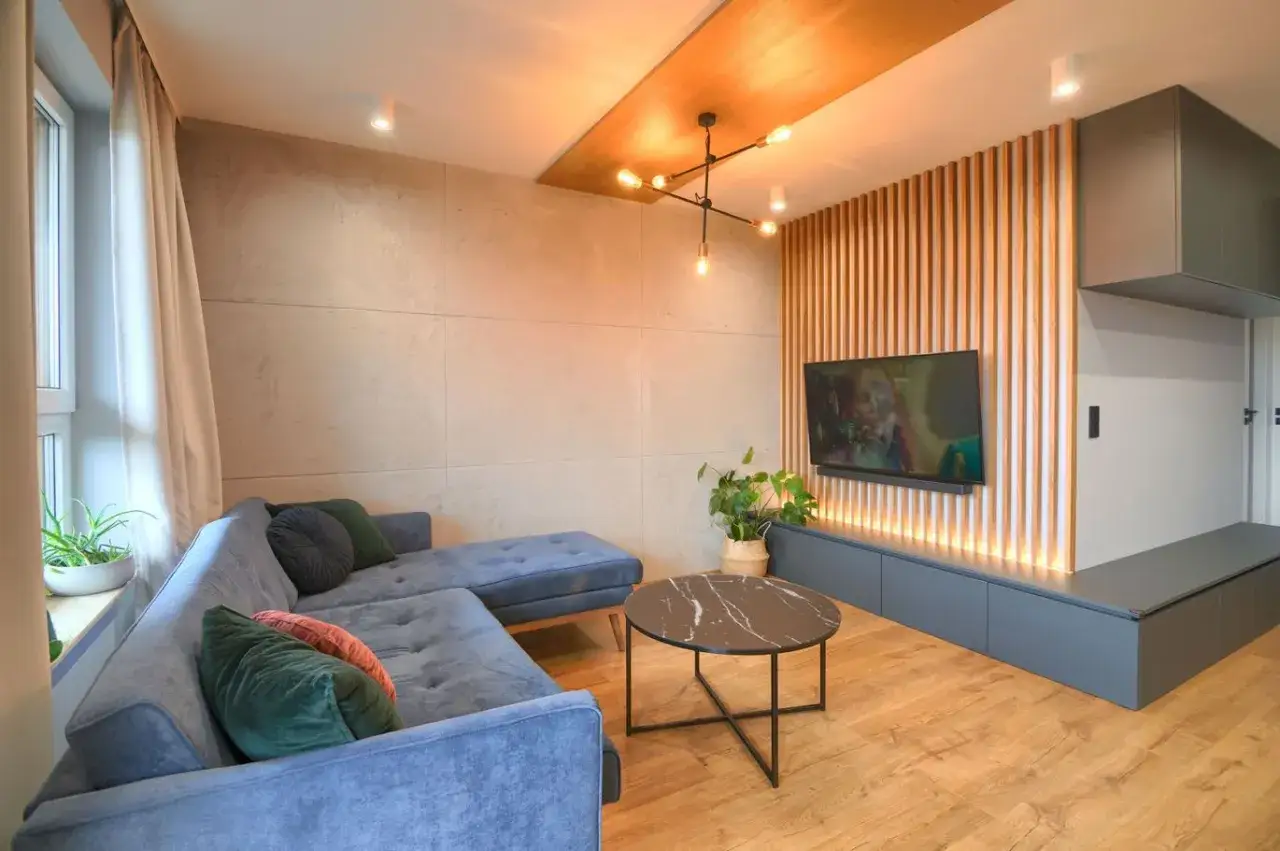 Nowoczesny salon z sofą, stolikiem kawowym i telewizorem. Beton w salonie aranżacja wnętrz z drewnianymi elementami i designerskim oświetleniem.