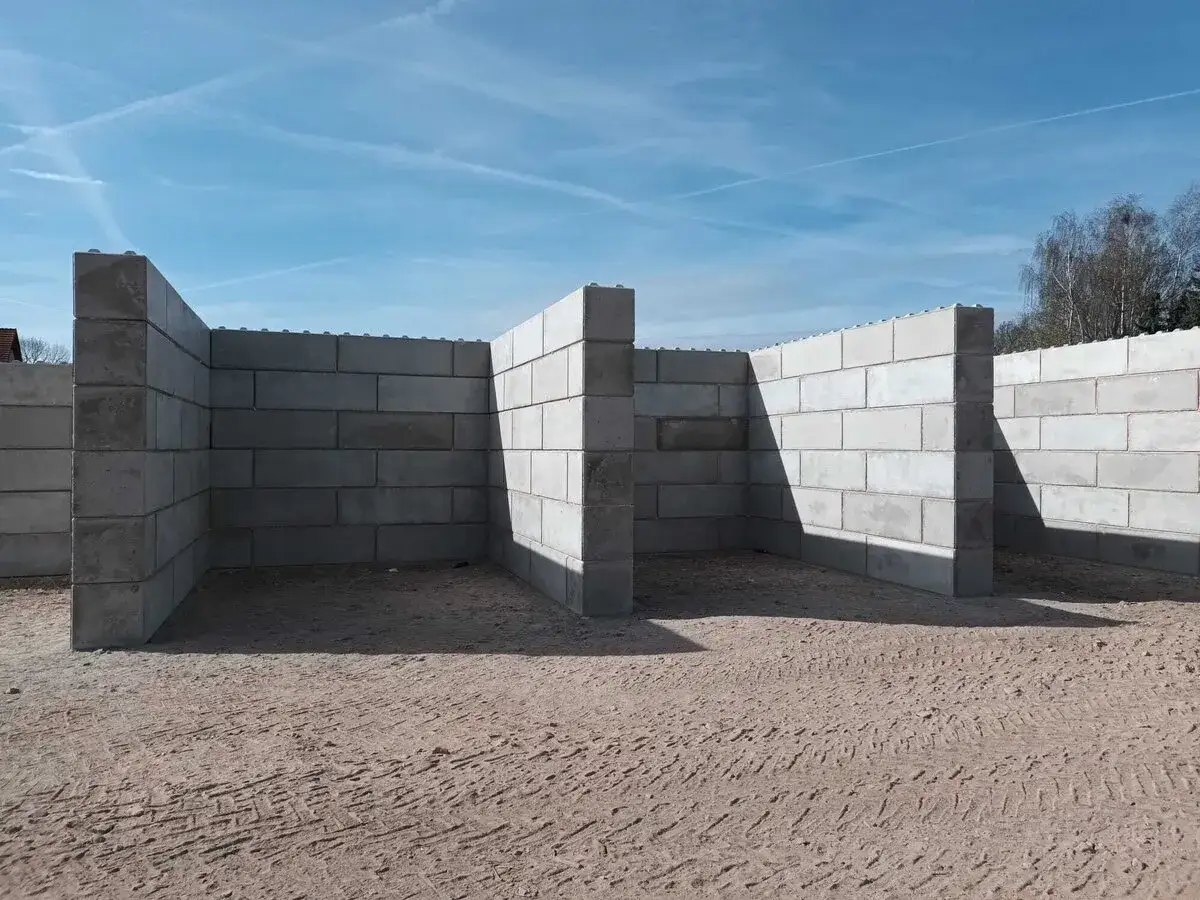 Budowa muru oporowego z bloczków betonowych. Konstrukcja w kształcie litery L, z widocznymi słupkami wzmacniającymi.